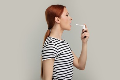 Young woman using throat spray on grey background
