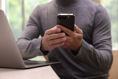 Photo of Man sending message via smartphone at table indoors, closeup