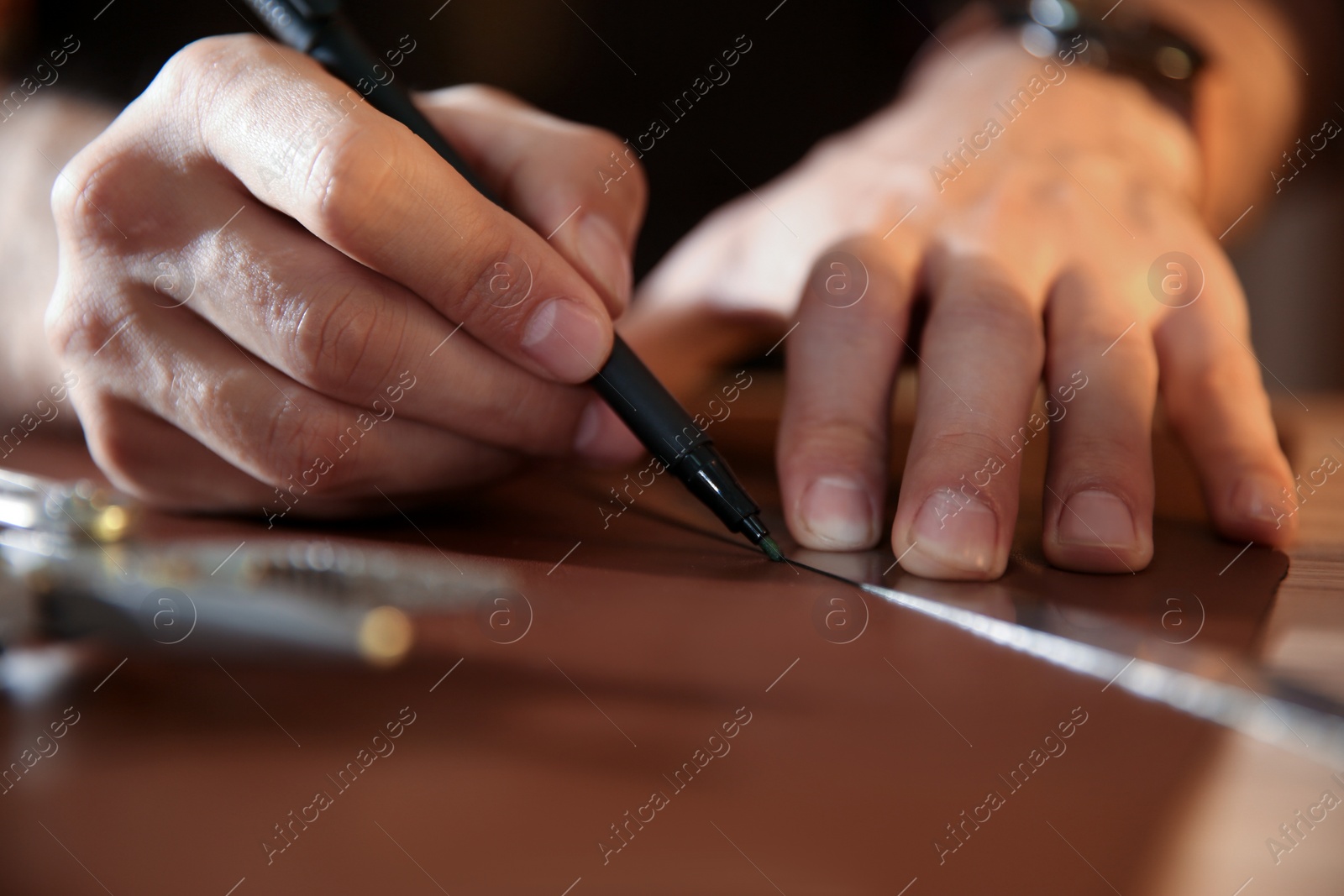 Photo of Man working with piece of leather at table, closeup