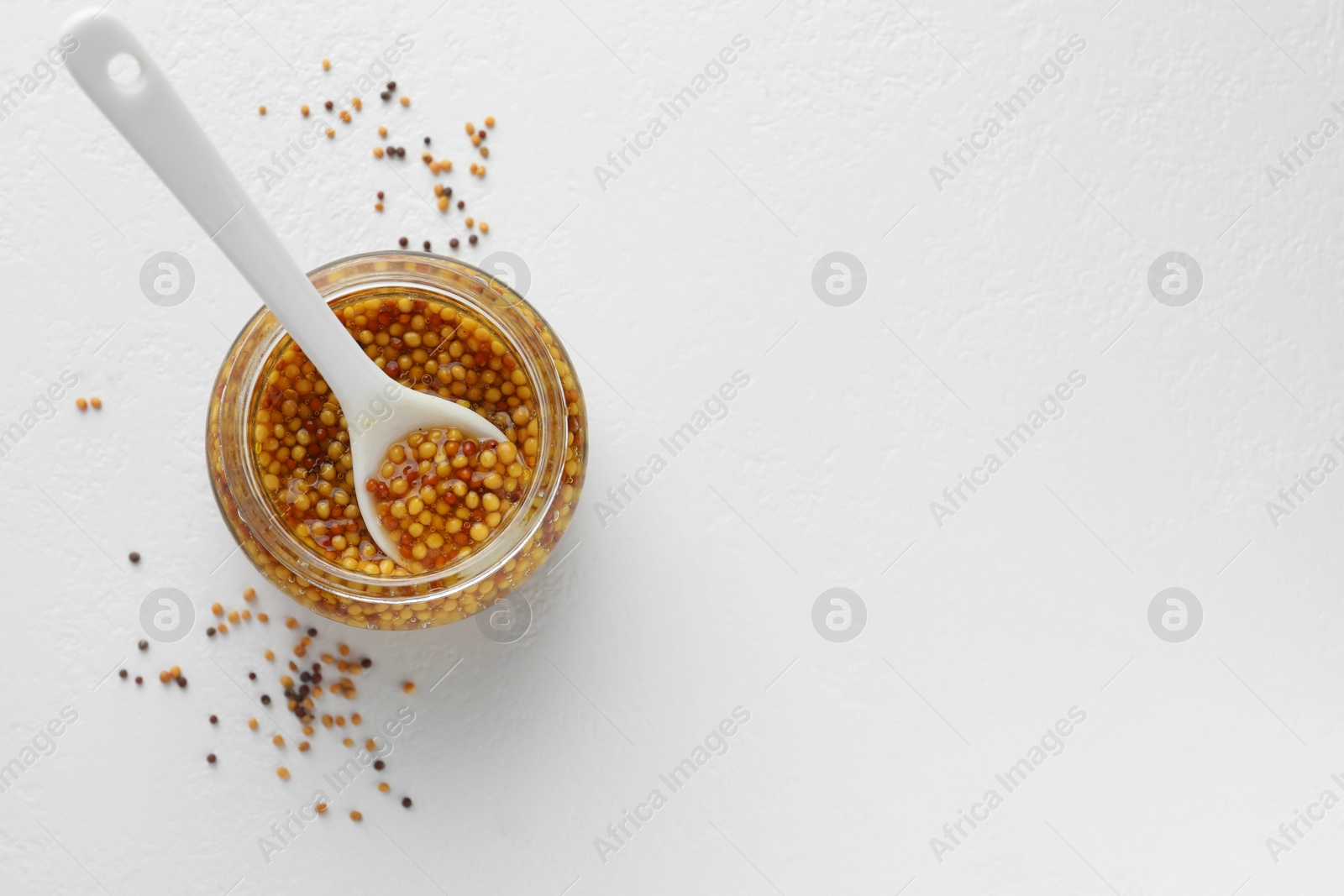 Photo of Whole grain mustard in jar and dry seeds on white table, flat lay. Space for text