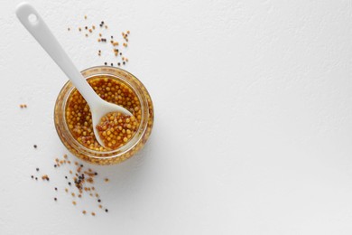 Whole grain mustard in jar and dry seeds on white table, flat lay. Space for text