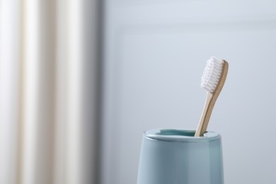 Bamboo toothbrush in holder on blurred background, closeup. Space for text