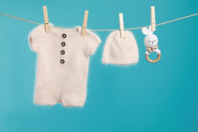 Knitted baby clothes and handmade toy drying on washing line against turquoise background