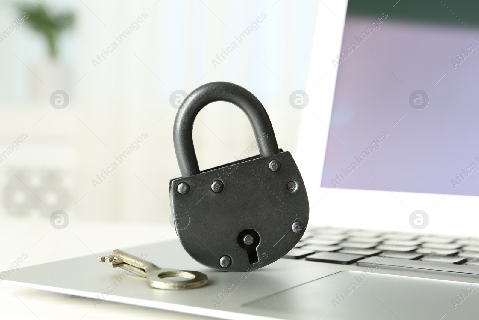 Photo of Vintage metal lock with key and laptop on table, closeup. Protection from cyber attack