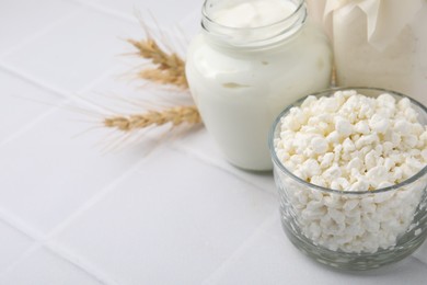 Photo of Different dairy products and spikes on white tiled table, space for text