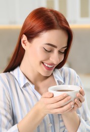 Photo of Happy woman with red dyed hair enjoying cup of drink in kitchen