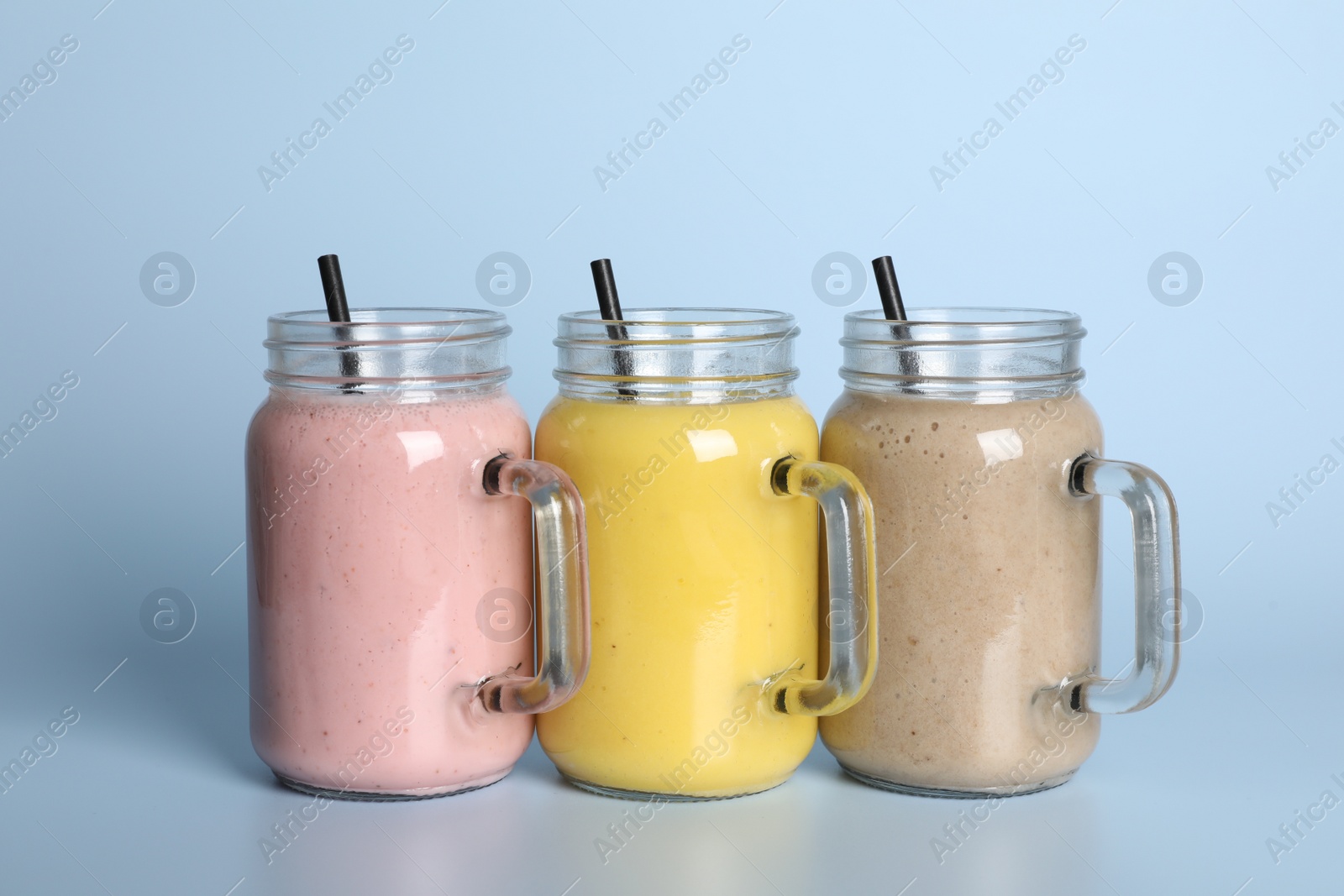 Photo of Mason jars with different smoothies on light blue background