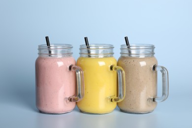 Photo of Mason jars with different smoothies on light blue background