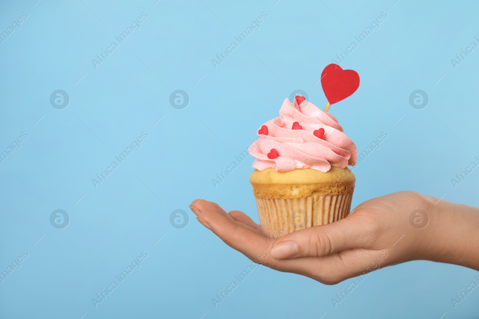 Photo of Closeup view of woman holding tasty cupcake on light blue background, space for text. Valentine's Day celebration