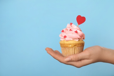Photo of Closeup view of woman holding tasty cupcake on light blue background, space for text. Valentine's Day celebration
