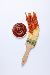 Photo of Brush painting with spaghetti dipped in ketchup on white background, top view. Creative concept