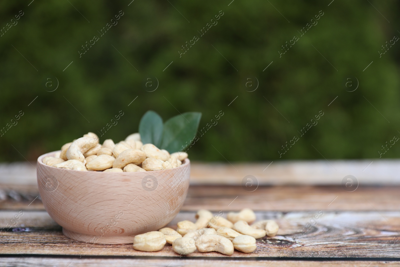 Photo of Tasty cashew nuts in bowl on wooden table outdoors, space for text