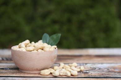 Tasty cashew nuts in bowl on wooden table outdoors, space for text