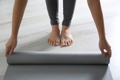 Woman rolling yoga mat on floor indoors, closeup