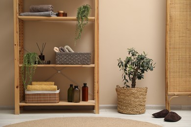 Photo of Shelving unit with soft towels, plants and bottles indoors
