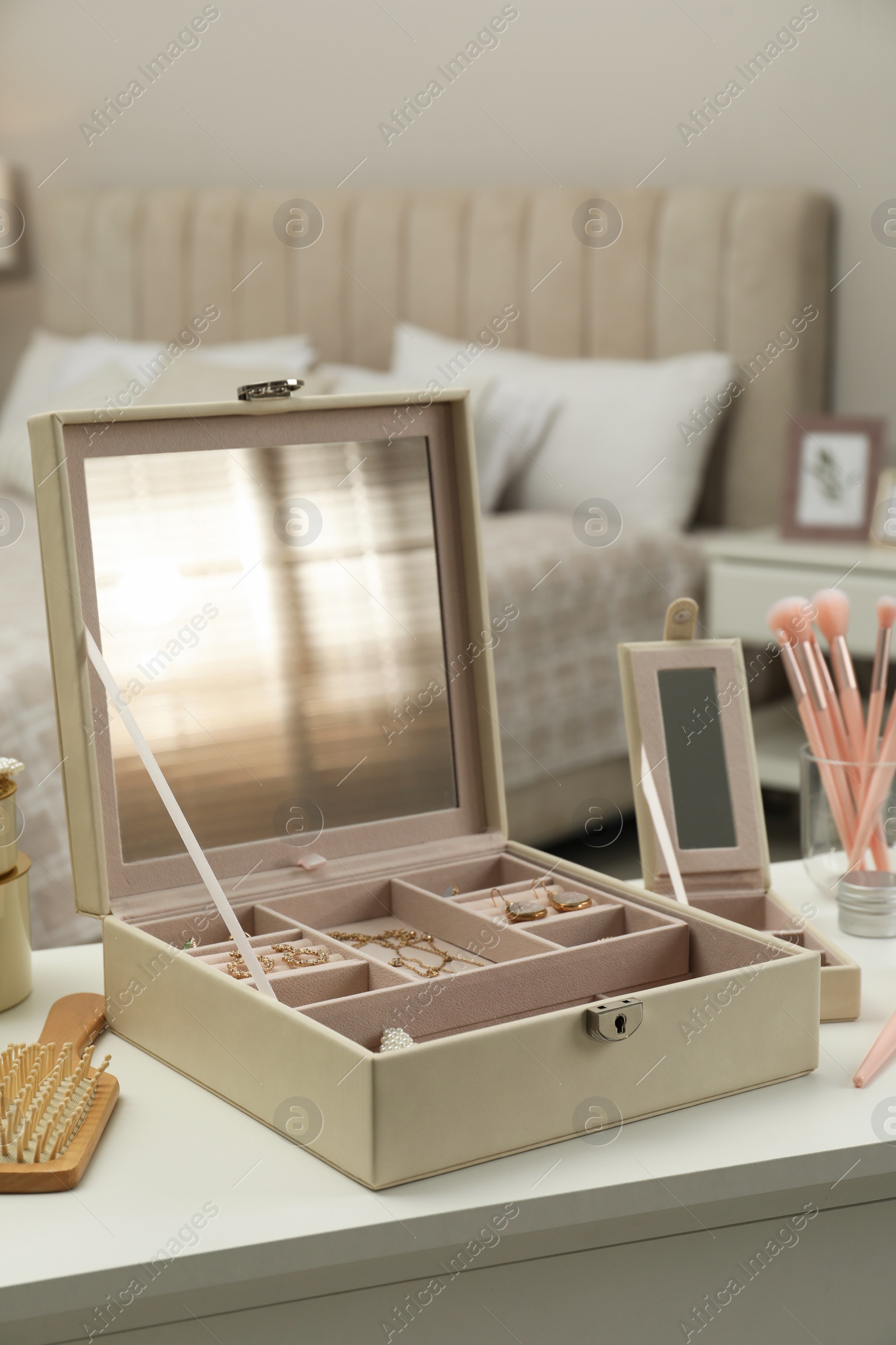 Photo of Elegant jewelry box with beautiful bijouterie and cosmetics on dressing table in bedroom