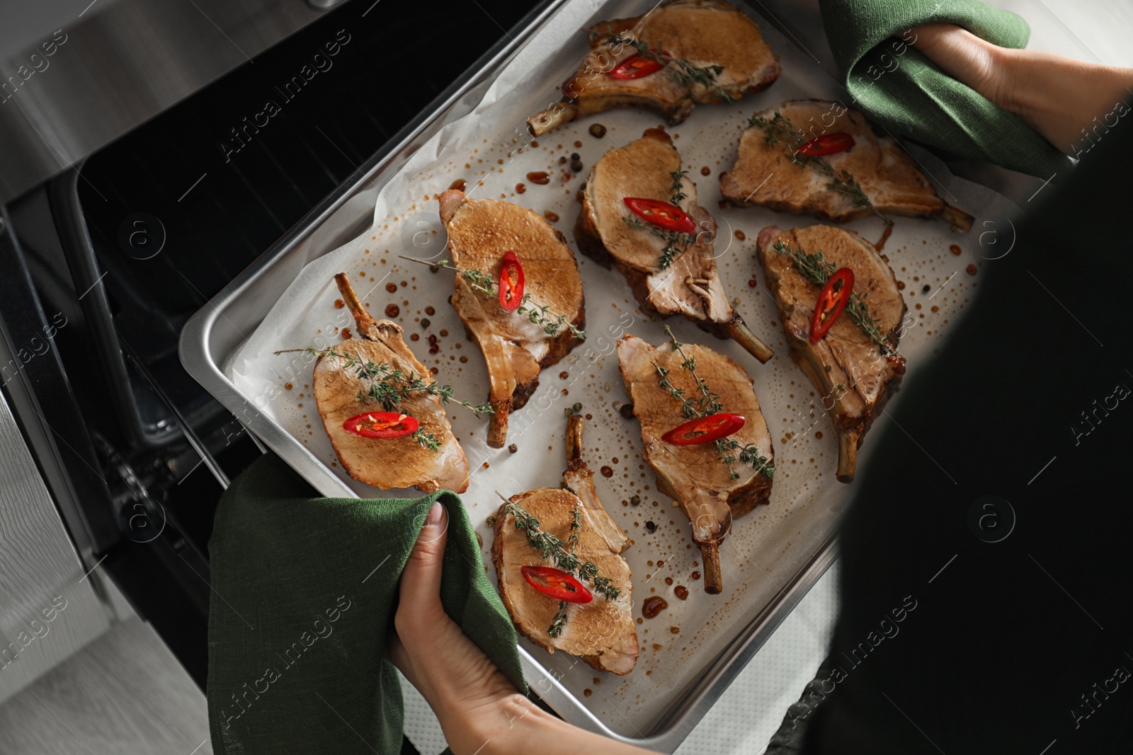 Photo of Woman taking delicious ribs out of oven, closeup