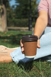 Photo of Woman holding takeaway cardboard coffee cup with plastic lid in park, closeup