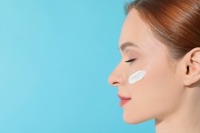 Photo of Beautiful young woman with sun protection cream on her face against light blue background, closeup. Space for text