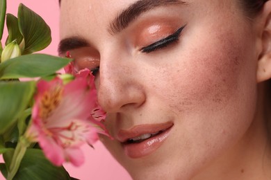 Photo of Beautiful woman with fake freckles and flower on pink background, closeup