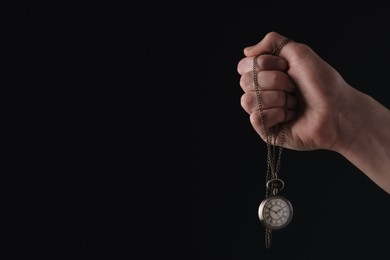 Man holding chain with elegant pocket watch on black background, closeup. Space for text