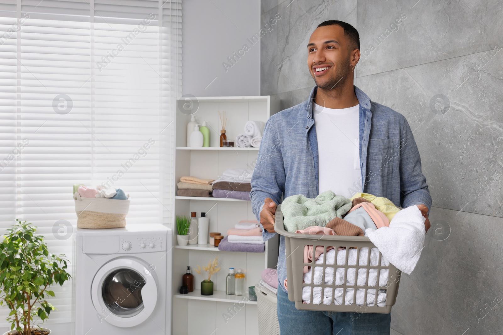 Photo of Happy man with basket full of laundry in bathroom. Space for text