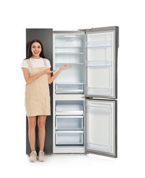 Young woman near empty refrigerator on white background