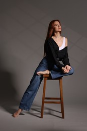 Photo of Beautiful young woman sitting on stool against gray background