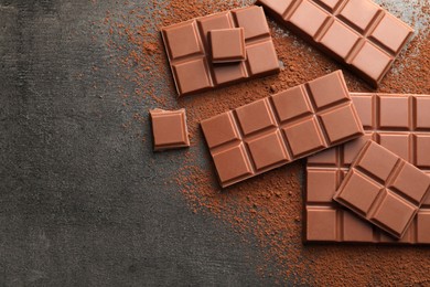 Photo of Delicious milk chocolate and cocoa powder on grey table, flat lay. Space for text