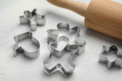 Cookie cutters, rolling pin and flour on white table, closeup
