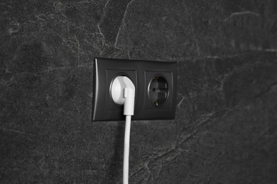 Photo of Power sockets with inserted plug on dark grey wall. Electrical supply