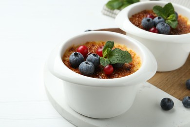 Delicious creme brulee with berries and mint in bowls on white wooden table, closeup. Space for text