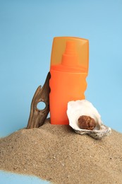 Photo of Sand with bottle of sunscreen, tree bark and seashells against light blue background. Sun protection