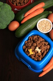 Photo of Dry pet food, products and vitamins on wooden background, above view