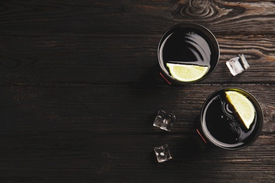 Photo of Refreshing soda drinks with ice cubes and lime on black wooden table, flat lay. Space for text