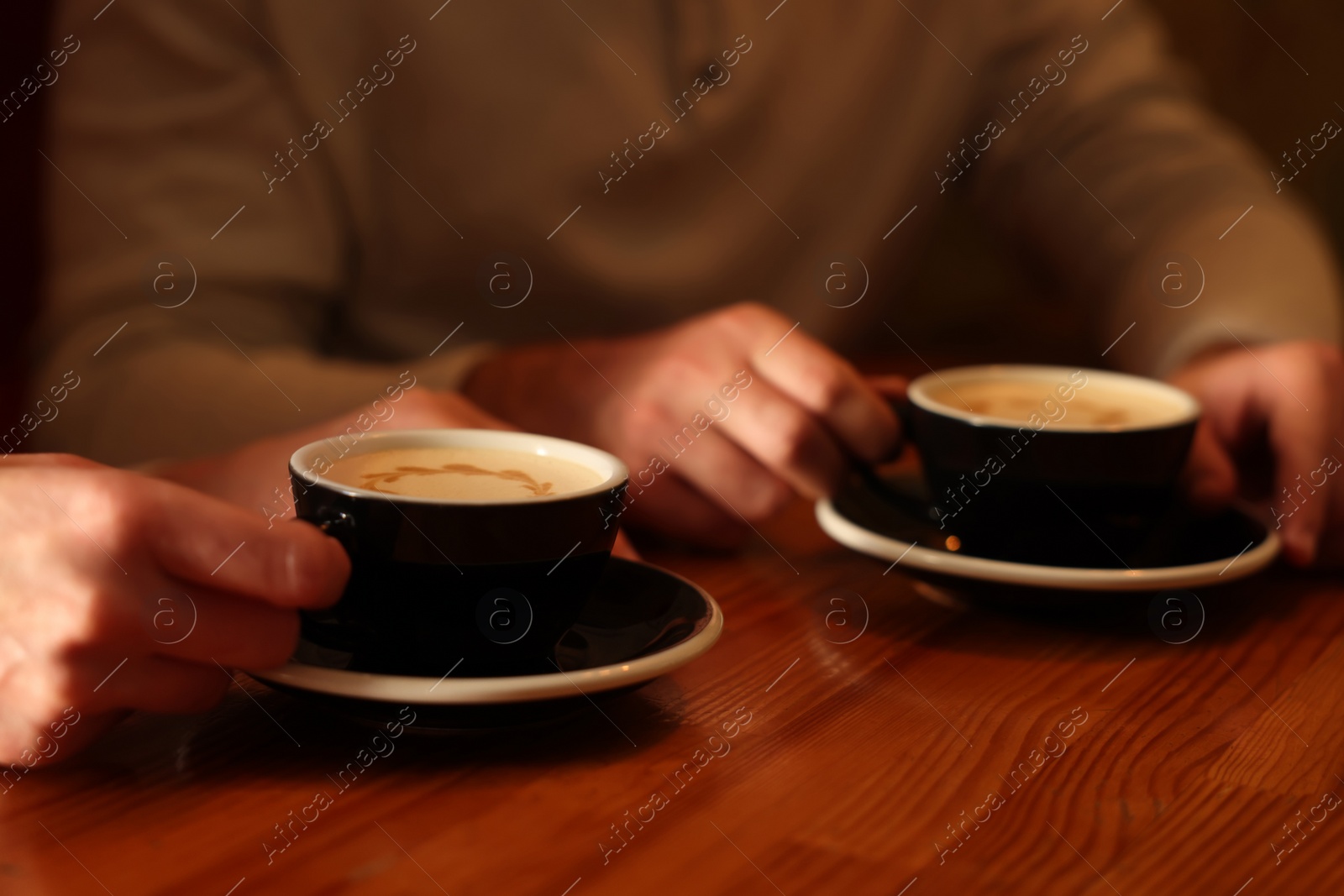 Photo of Couple with cups of aromatic coffee at wooden table, closeup