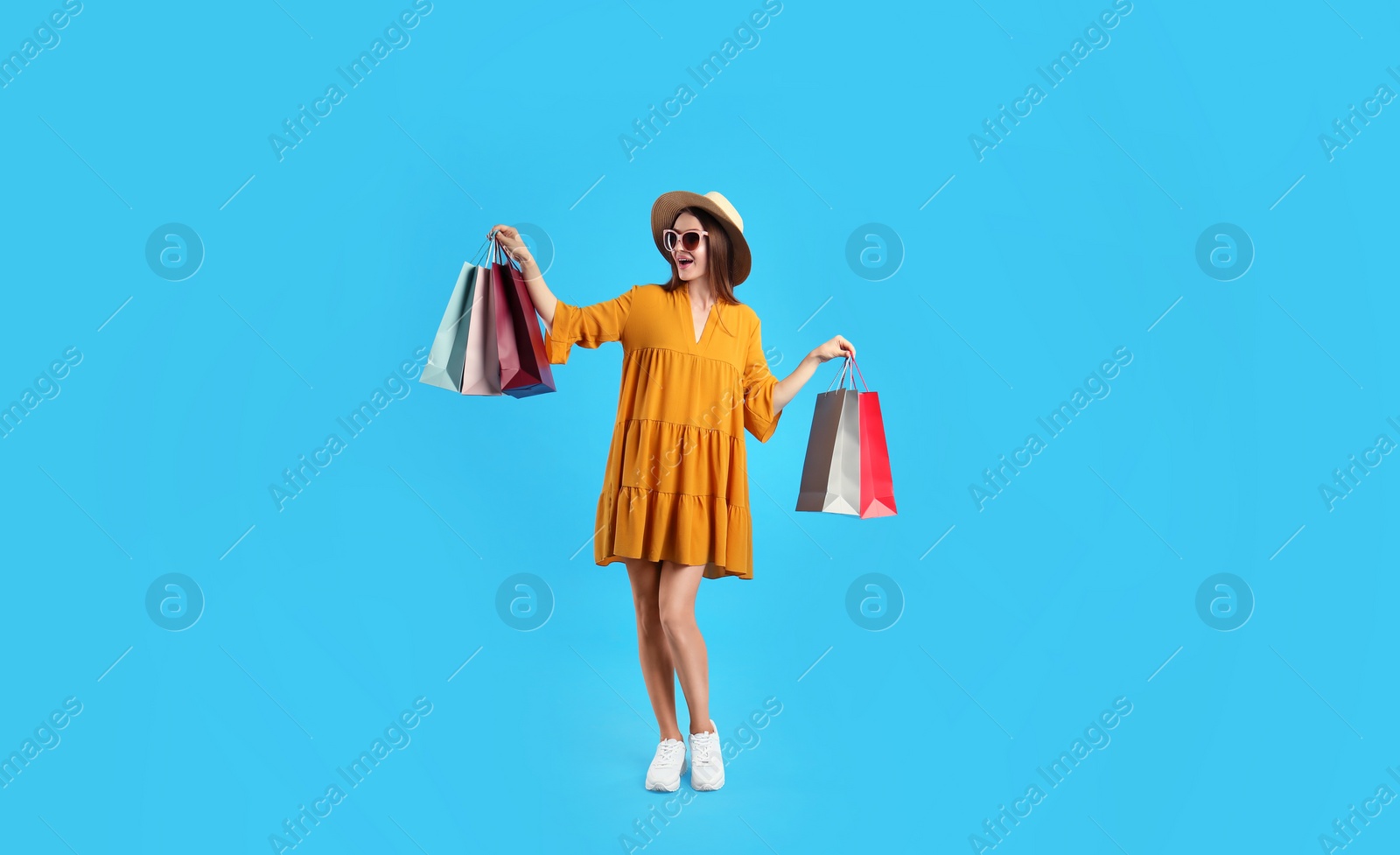 Photo of Beautiful young woman with paper shopping bags on light blue background