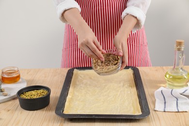 Making delicious baklava. Woman adding chopped nuts to dough at wooden table, closeup