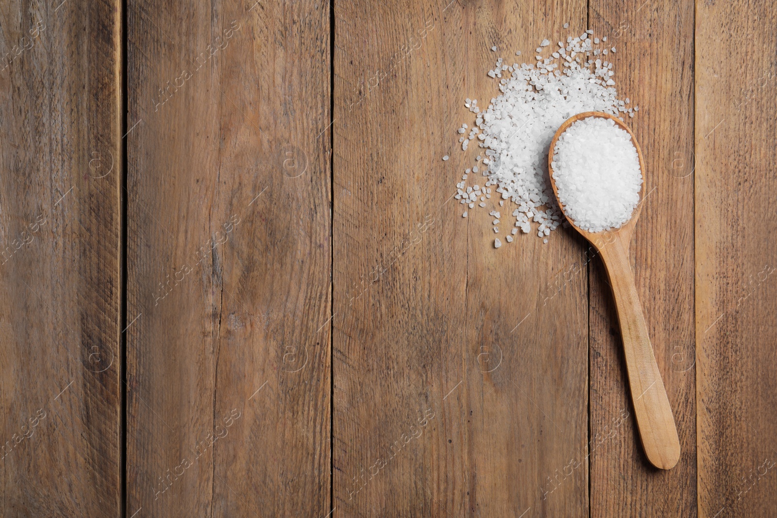 Photo of Spoon and heap of natural sea salt on wooden table, top view. Space for text