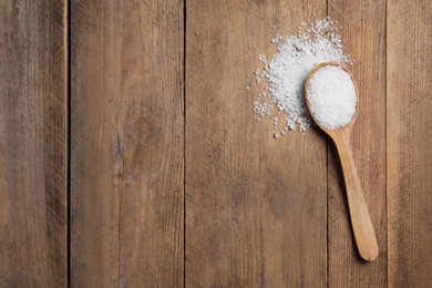 Photo of Spoon and heap of natural sea salt on wooden table, top view. Space for text
