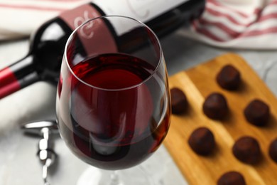 Photo of Glass of red wine with chocolate candies on light table, closeup