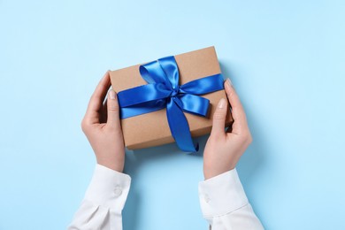 Photo of Woman holding gift box on light blue background, top view