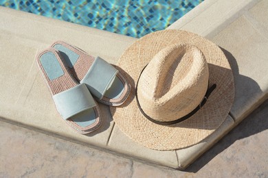 Photo of Stylish slippers and straw hat at poolside on sunny day. Beach accessories
