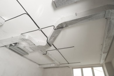 Photo of Conduits with cables and ventilation system on white ceiling, low angle view. Installation of electrical wiring