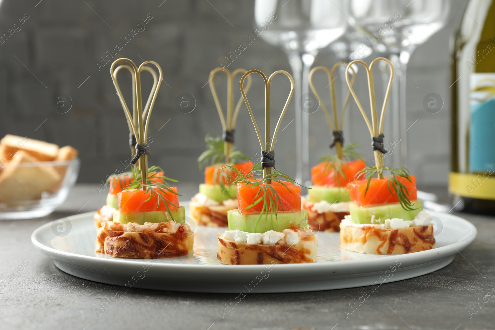 Photo of Tasty canapes with salmon, cucumber, bread and cream cheese on grey table