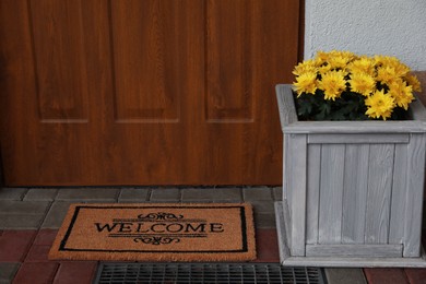 Photo of Doormat with word Welcome and beautiful flowers on floor near entrance