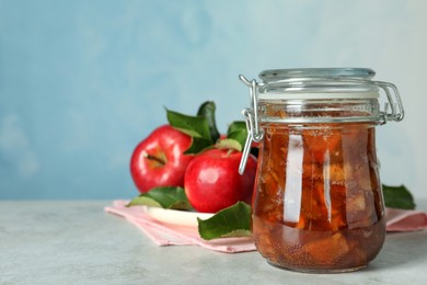 Photo of Tasty apple jam in glass jar and fresh fruits on light table, space for text