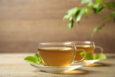 Photo of Cups of green tea and leaves on wooden table