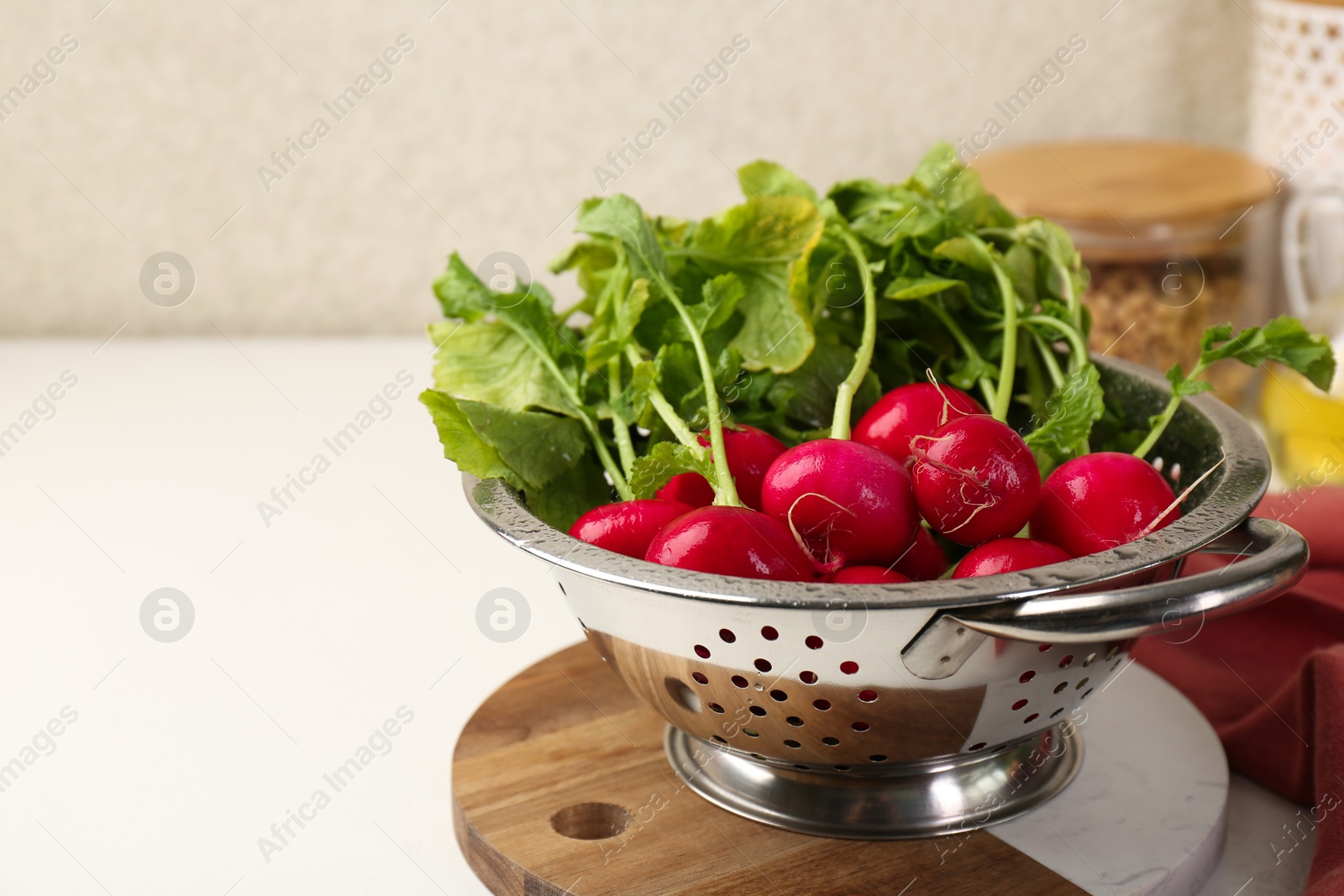 Photo of Wet radish in colander on white table, closeup. Space for text