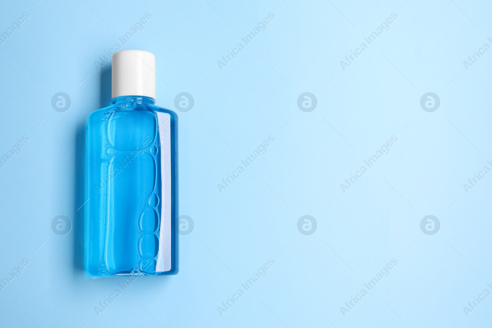 Photo of Fresh mouthwash in bottle on light blue background, top view. Space for text